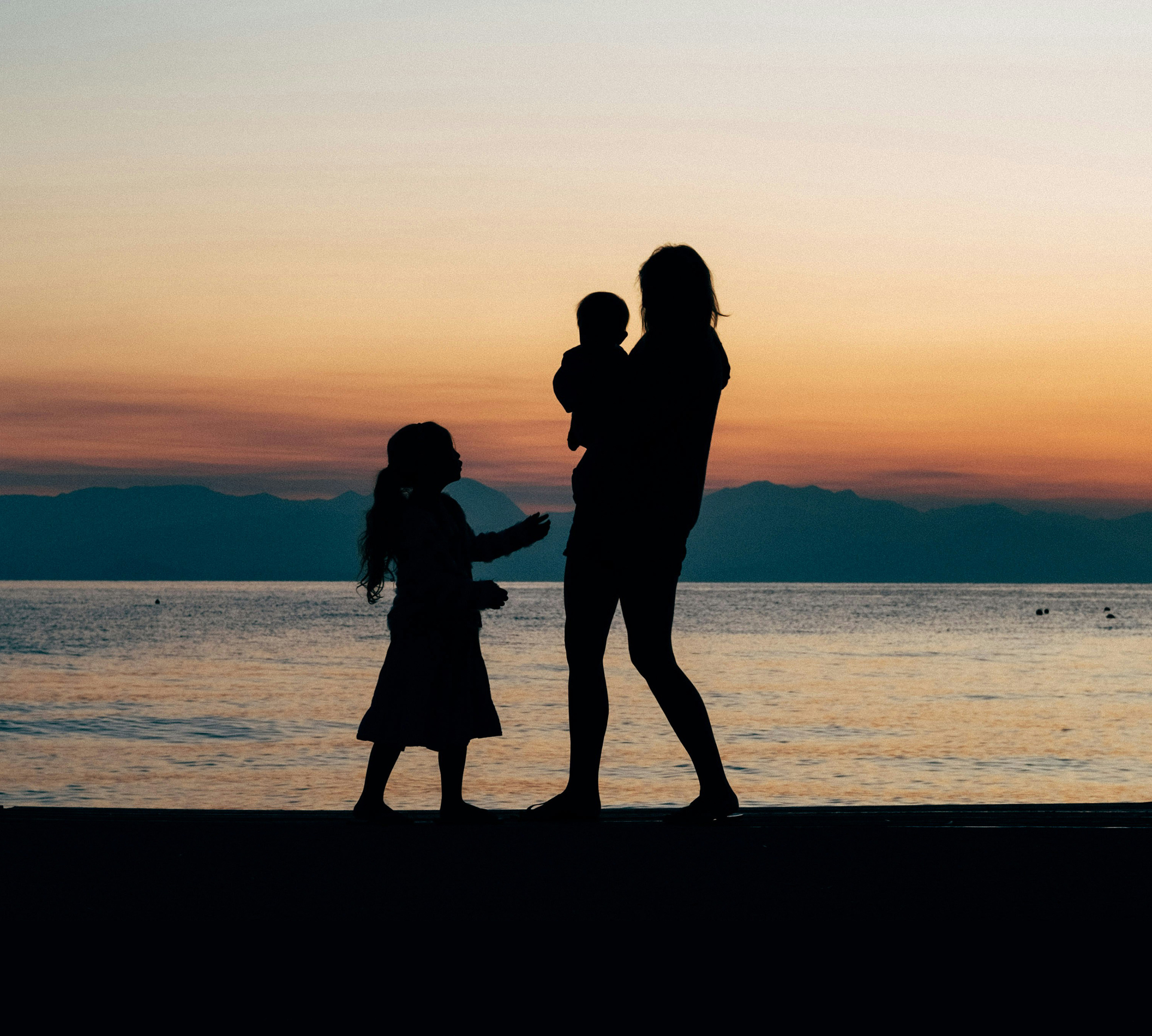 a silhouette of a person holding a baby and a child on a beach